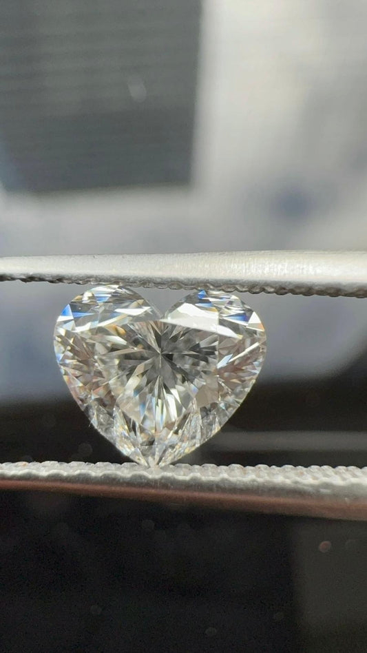 Loose heart-shaped diamond held in metal tweezers, displaying exceptional brilliance and precise symmetrical faceting against a soft dark background.